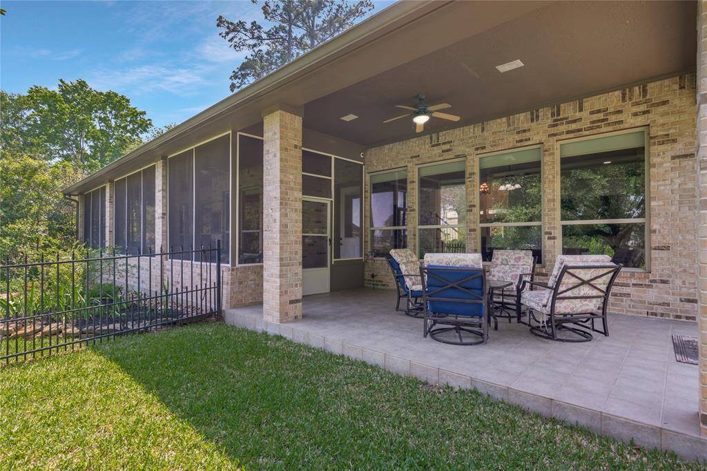 This photo shows a spacious, patio with comfortable outdoor seating and a ceiling fan. It features brick walls and overlooks a lush, green yard, offering a perfect space for relaxing or entertaining.