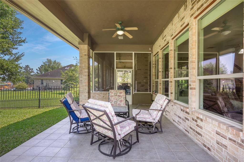 This photo showcases a spacious covered patio with tiled flooring, comfortable seating, and a ceiling fan for added comfort. It overlooks a green lawn with a view of neighboring houses, offering a serene outdoor living space.
