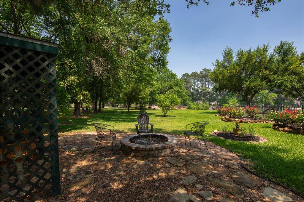 This photo showcases a spacious, lush backyard with a charming fire pit area surrounded by chairs, mature trees, and well-maintained flower beds, offering a serene outdoor retreat.