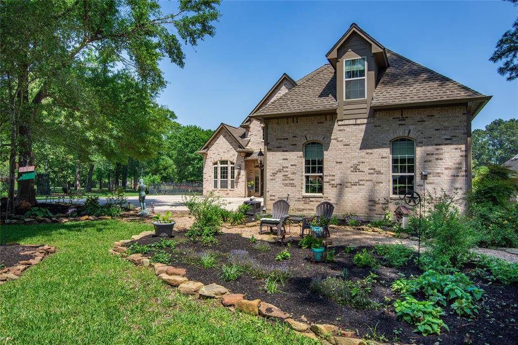 Charming brick home with a beautifully landscaped front yard featuring a variety of plants and a cozy seating area. The property is surrounded by lush greenery, providing a serene and private atmosphere.