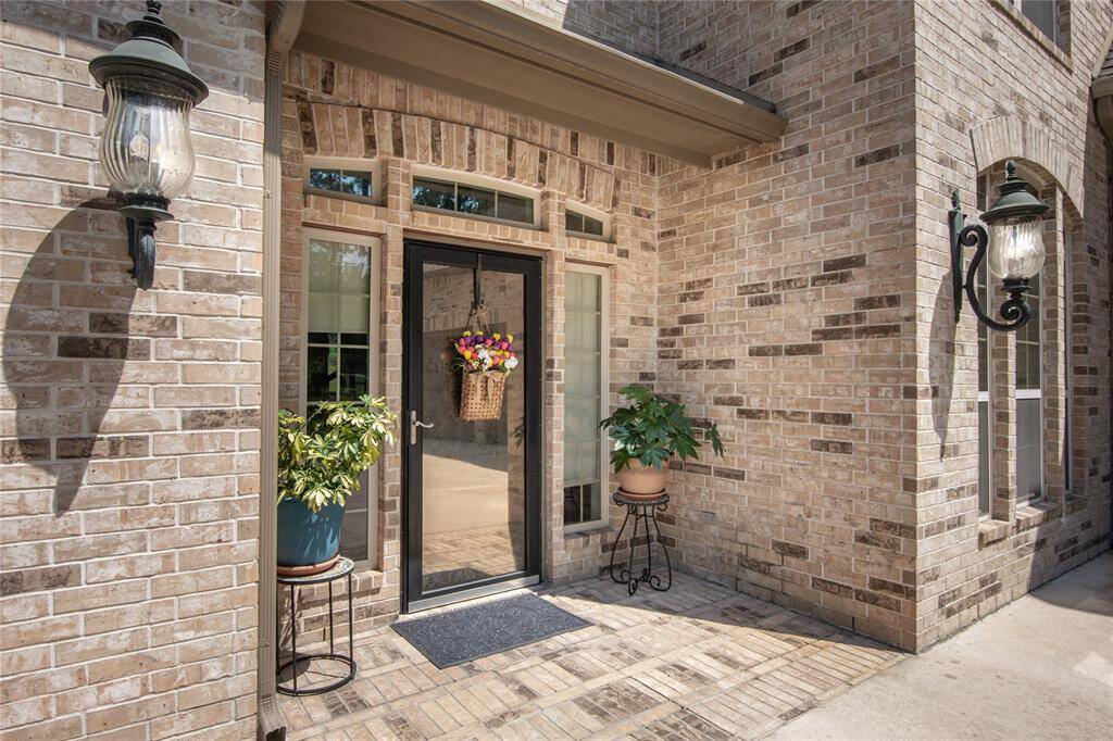This photo showcases a charming brick home entrance with a black-framed glass door flanked by sidelights. Elegant outdoor sconces provide lighting, and potted plants add a welcoming touch to the entryway.