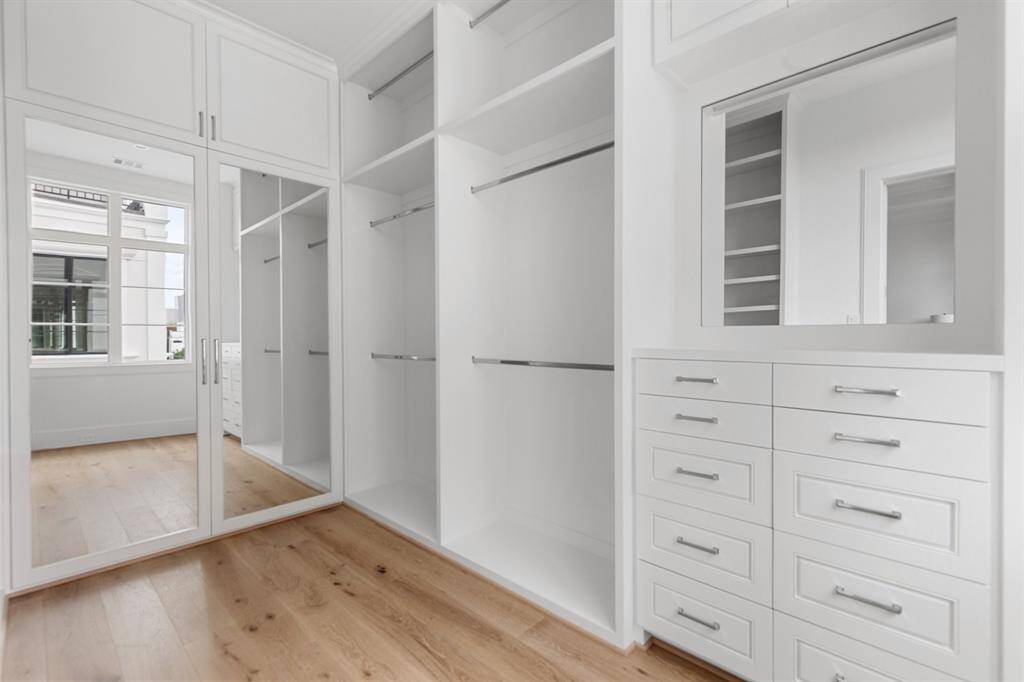 The spacious walk-in closet features elevated features such as furniture style cabinetry, adjustable shelves, a vanity area with specialized accessory storage, valet rods, and more