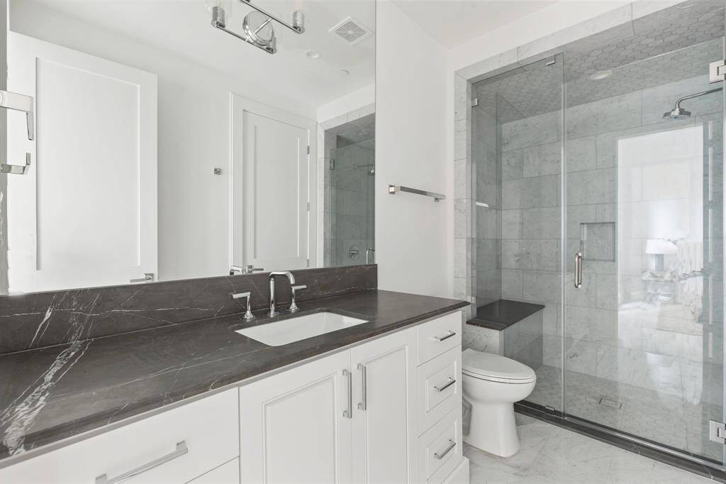 The en suite ground floor bathroom features a stone countertop with furniture-style cabinetry and a frameless glass walk-in shower with bench seating.