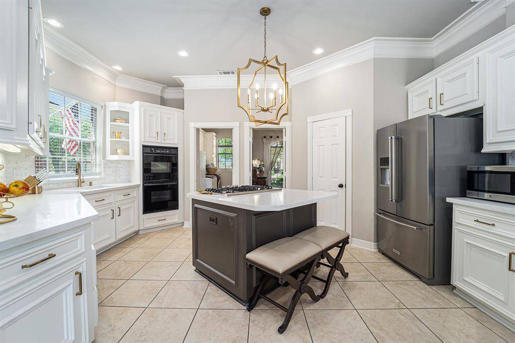 This stunning kitchen also showcases double ovens, a center island with a built-in cooktop, and a statement chandelier!