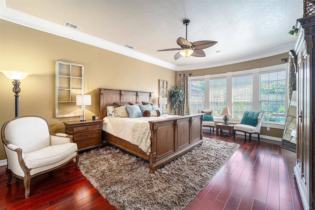 This spacious primary bedroom offers a peaceful retreat with abundant natural light, elegant crown molding, and a cozy sitting area overlooking the backyard.