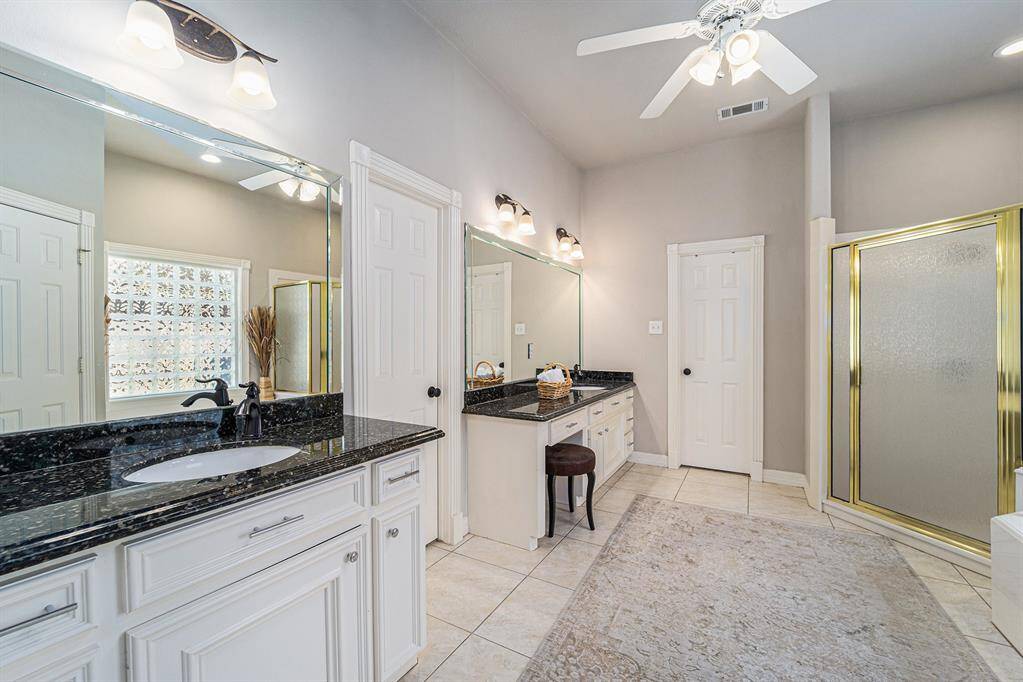 The expansive primary bathroom features dual vanities with sleek countertops, vanity seating, and dual walk-in closets.
