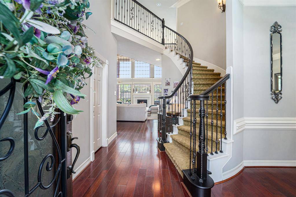 Welcome guests in style with this breathtaking foyer showcasing beautiful floors, a curved staircase with wrought iron accents, and an open view into the bright and inviting living space.