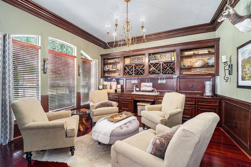 This sophisticated flex space is currently styled as a wine room, featuring custom built-ins, rich wood cabinetry, elegant lighting, and a wall of arched windows that flood the room with natural light.
