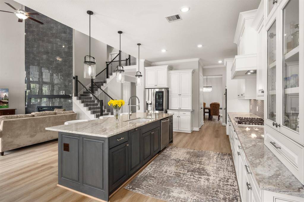 Stunning white cabinetry is complemented by gorgeous granite countertops, an appliance garage, and a stylish grey-glazed island with pendant lighting and eat-in bar seating.