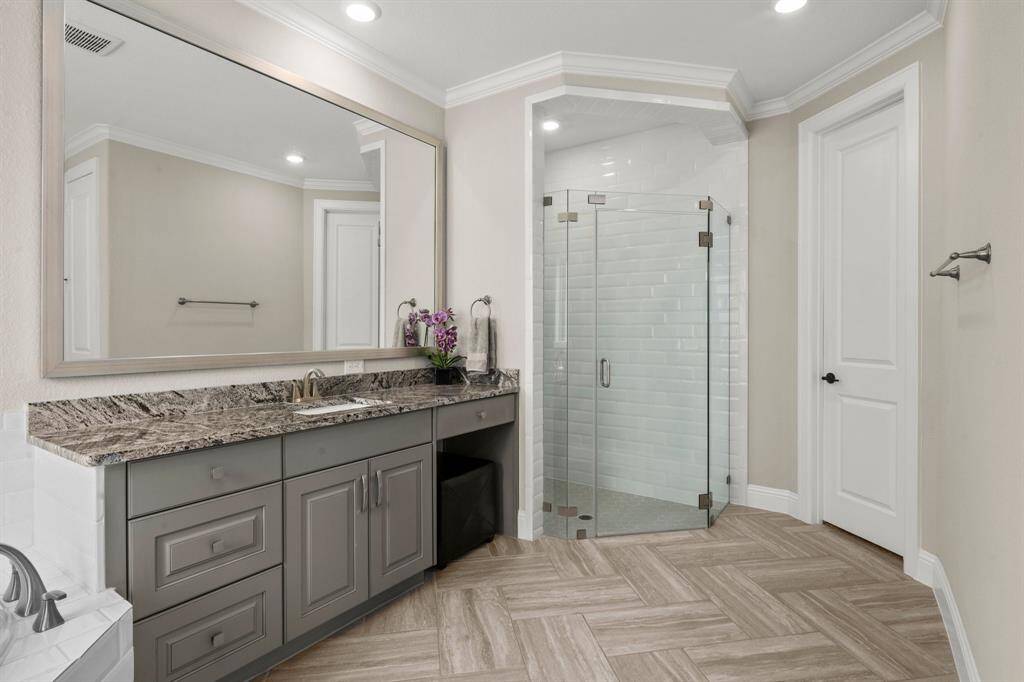 Herringbone-patterned tile flooring adds flair to this spa-like bathroom. Dual vanities—one with a sitting area—are topped with beautiful granite and framed mirrors.