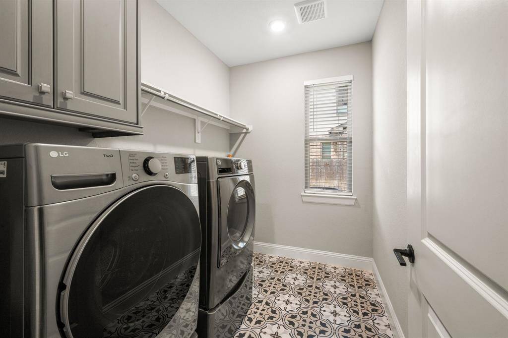 This laundry room includes cabinets for storage, decorative tile flooring, and a window for natural light. A refrigerator connection offers extra flexibility for busy households.