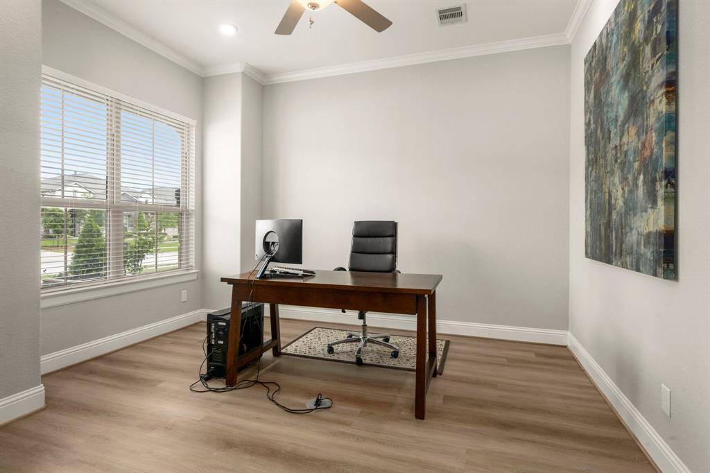 The home office is a quiet retreat tucked just off the entry, complete with crown molding, a ceiling fan, and a large window that frames a peaceful view of the front yard—perfect for working in style and comfort.