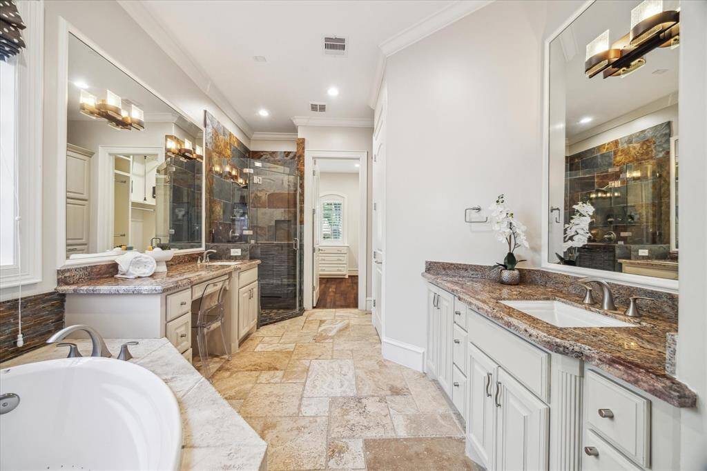 The spa-like primary bathroom features a luxurious soaking tub, a spacious walk-in shower with elegant tile, and dual vanities with granite countertops.