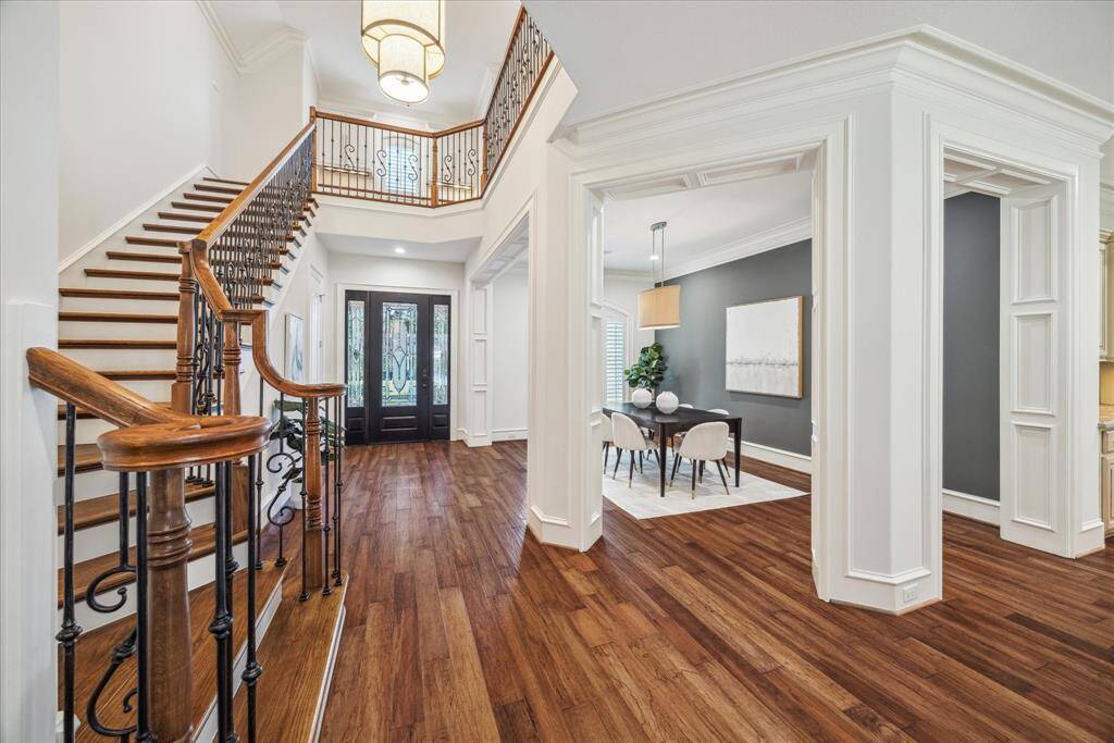 The grand entry is complemented by a stunning staircase that serves as a focal point, featuring elegant wood steps and a sleek iron railing. The open, airy feel of the space is enhanced by soaring ceilings.