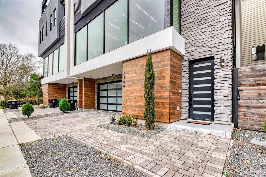 This modern home features a sleek exterior with large windows, mixed materials including wood and stone accents, and a stylish entryway. The driveway and walkway are paved with contemporary landscaping, offering a clean and sophisticated curb appeal.