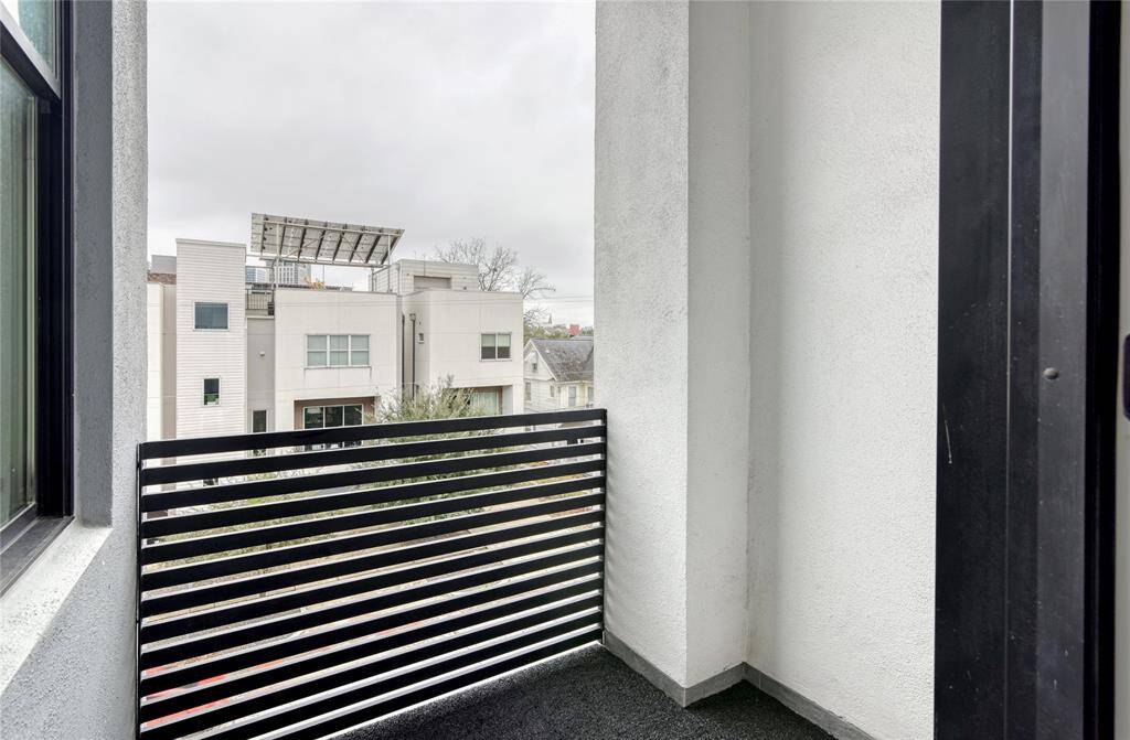 This photo shows a small, modern balcony with a sleek black railing, offering a view of nearby contemporary buildings. It's a cozy outdoor space for relaxation or enjoying the view.