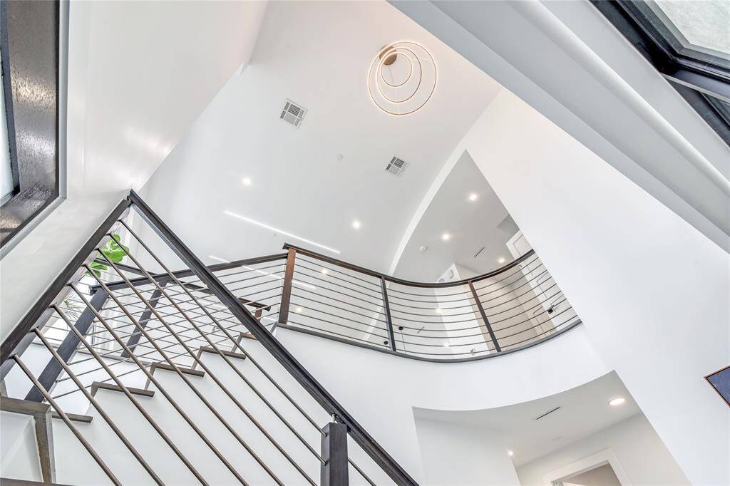 This photo showcases a modern, open staircase with sleek metal railings and a unique spiral light fixture above. The space is bright and airy, featuring high ceilings and contemporary design elements.