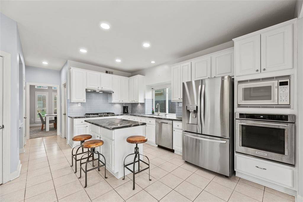 Sleek tile backsplash complements gleaming stainless steel appliances. Recessed lighting. this is an easy kitchen to move around and create.