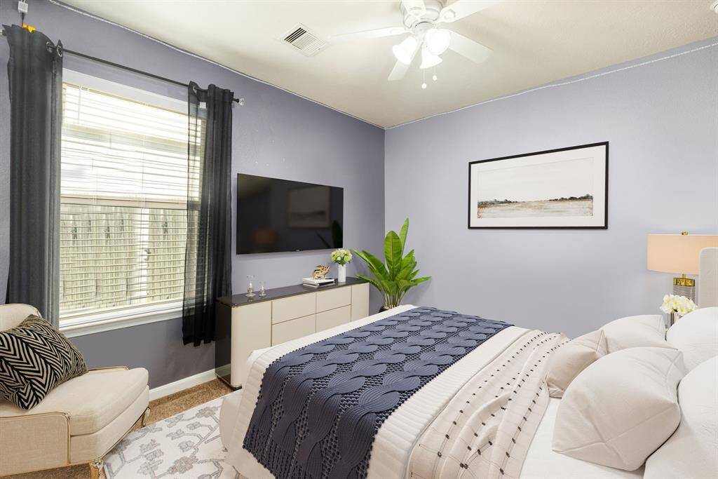 Secondary bedroom features plush carpet, custom paint, ceiling fan with lighting and a large window with privacy blinds.