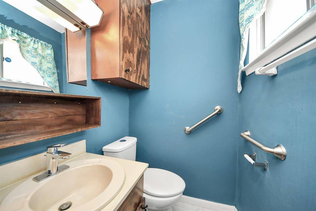 Half bathroom features a vanity and sink, a large mirror, and overhead lighting. It also includes a window for natural light.