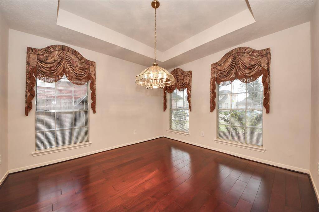 Formal Dining at the right of the entrance with rich hardwood floors, a tray ceiling, and a central chandelier. T
