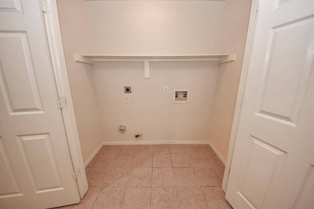 Laundry room with hookups for a washer and dryer. It features tiled flooring, a shelf for storage, and is enclosed by white doors.