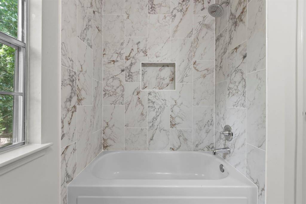 A luxurious spa-inspired shower-tub retreat, featuring elegant tile work and a bright window that invites natural light.