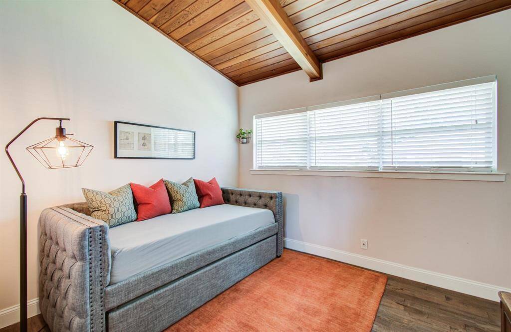 This spacious secondary bedroom is filled with natural light, thanks to a large window that brightens the entire space. A warm wooden ceiling with a beam adds character and a sense of coziness, complementing the room’s generous layout and inviting atmosphere. It’s a versatile space that offers both comfort and style.