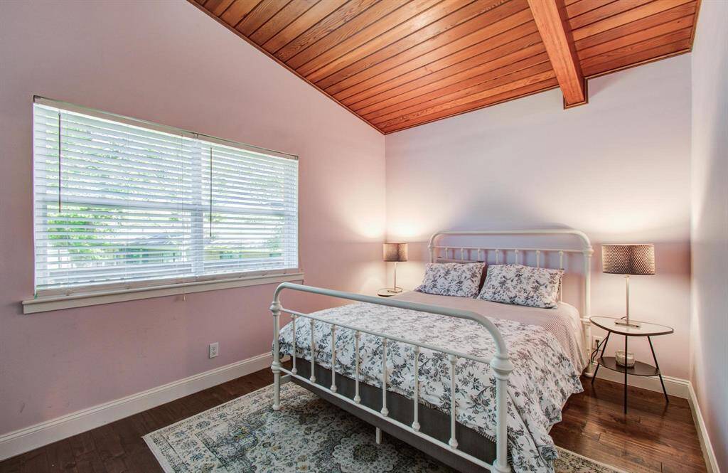 This spacious bedroom features a wooden ceiling, neutral colored walls, and a large window that fills the room with natural light. The combination of space, warmth, and charm makes it ideal for a child’s room or a generously sized shared office.