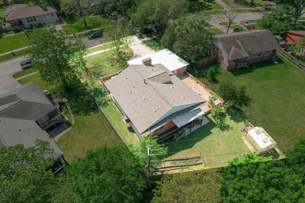 This aerial view showcases a charming home with a spacious backyard, surrounded by greenery and neighboring houses. The property features a recently replaced roof, a cozy patio area, and ample lawn space, ideal for outdoor activities and gardening. Situated in a quiet neighborhood with tree-lined streets, it offers a peaceful residential setting.