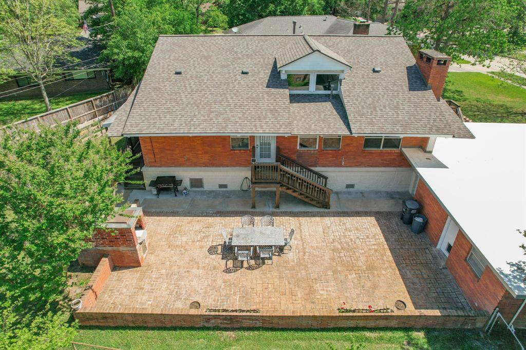 This aerial view showcases a spacious side yard with a large brick patio, perfect for outdoor dining and entertaining. The home features a classic brick exterior with a gabled roof, surrounded by lush greenery for added privacy. The door on the right leads into the garage which features a full bathroom.