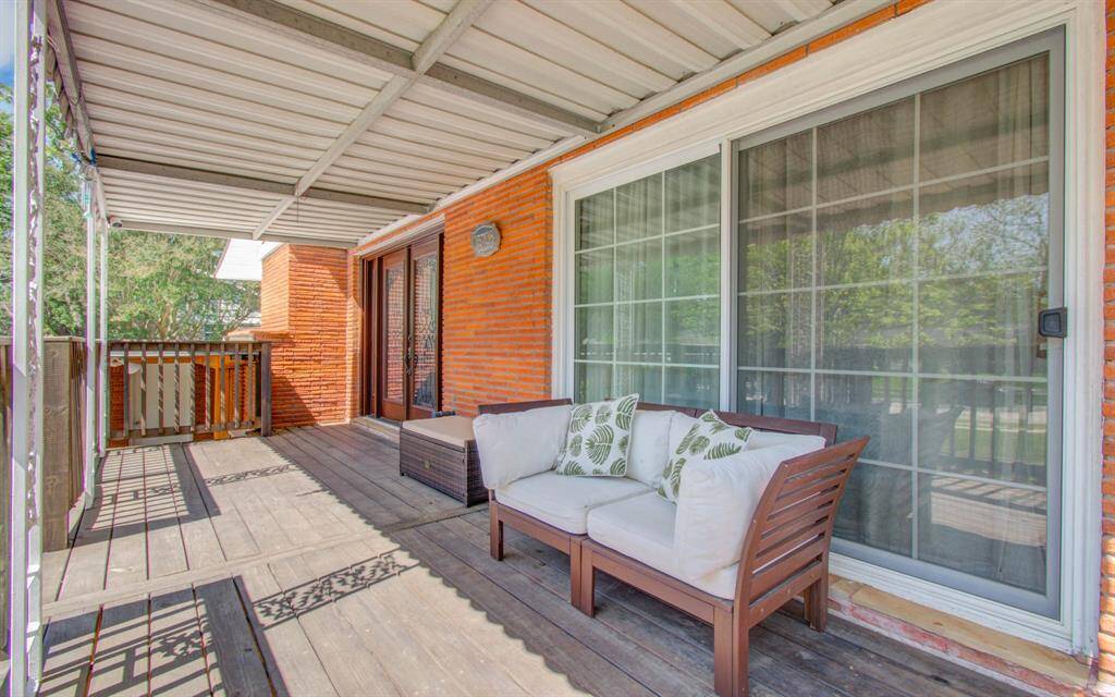 This inviting outdoor space features a covered wooden deck with comfortable seating and sliding glass doors, perfect for relaxing and enjoying the view.