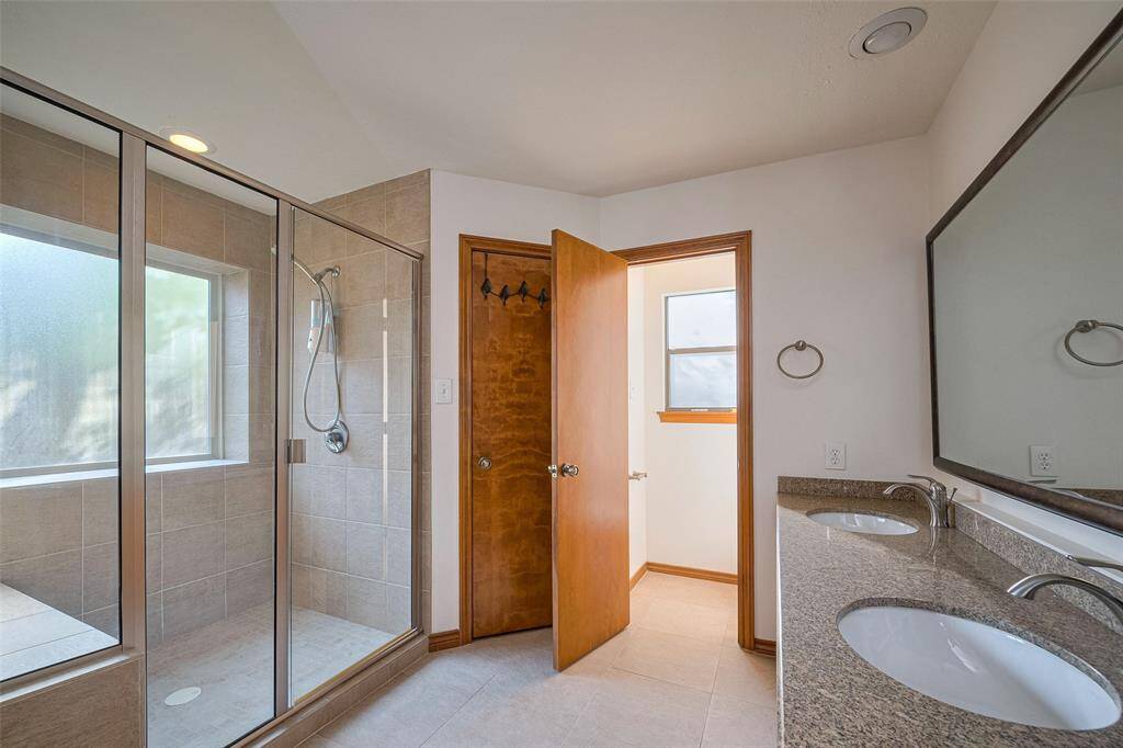 Spacious primary bath offers a luxurious glass-enclosed shower with a built-in bench, double vanities, and convenient access to two generously sized walk-in closets. It also features abundant natural light from the wide frosted window panel for added privacy.