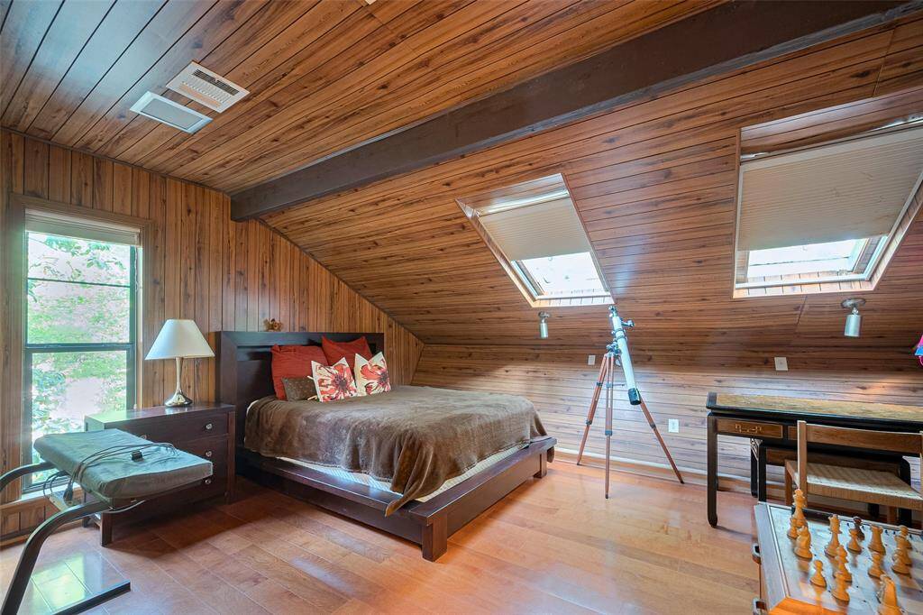 This unique, tucked-away bedroom showcases charming wood-paneled walls, skylight windows that fill the space with natural light, and its own private en-suite bath—offering both character and comfort.