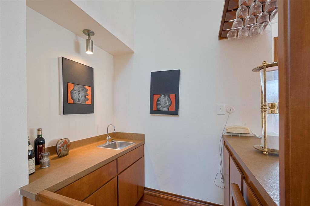 The wet bar, conveniently located near the main living, presents spacious countertops, a built-in sink, ample storage, and an overhead wine glass rack. It serves as the perfect support area for entertaining.