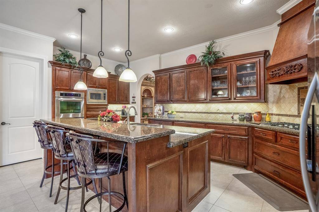 The gourmet kitchen features rich wood cabinetry & large venthood, granite countertops, and a central island anchoring the heart of the home. Stainless steel appliances, including double ovens, add functionality, while pendant lighting enhances the space. Notice the hidden appliance storage under the microwave - a necessary upgrade!