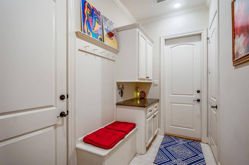 A well-organized mudroom with a large storage bench, hanging hooks & additional cabinets with a countertop is conveniently located between the two separate garage entrances, making it the perfect drop zone.