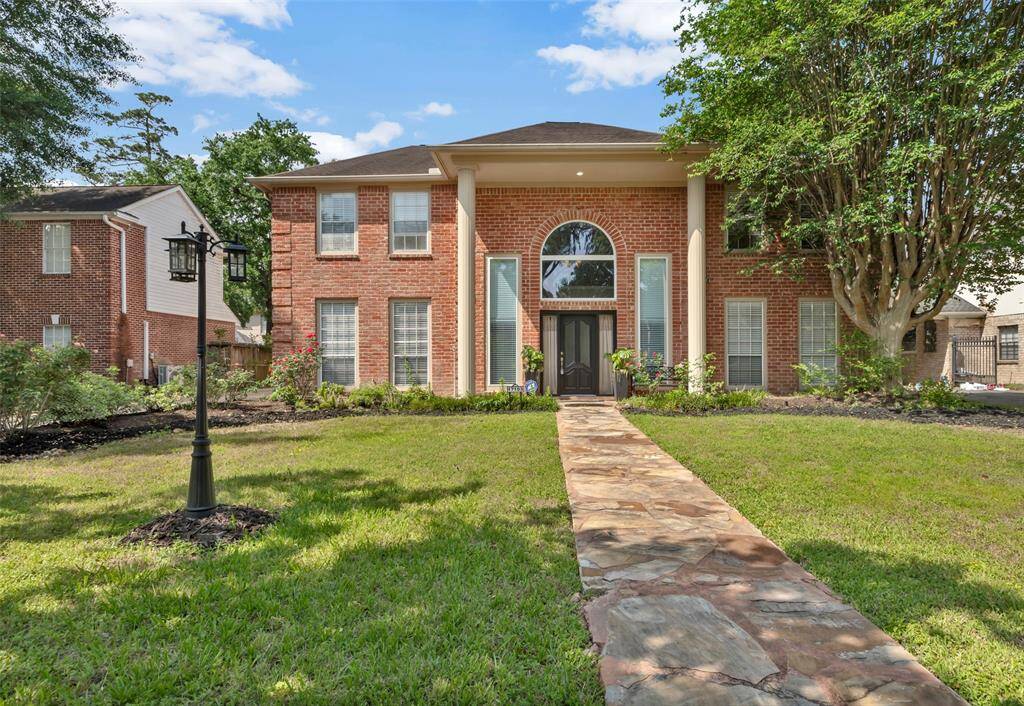 This elegant two-story brick home features a grand entrance with large pillars and a beautifully landscaped front yard. A stone path leads to the front door, framed by tall windows that offer ample natural light. Perfect for those seeking a classic and inviting curb appeal.