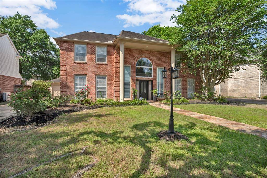 This elegant two-story brick home features a grand entrance with large pillars and a beautifully landscaped front yard. A stone path leads to the front door, framed by tall windows that offer ample natural light. Perfect for those seeking a classic and inviting curb appeal.