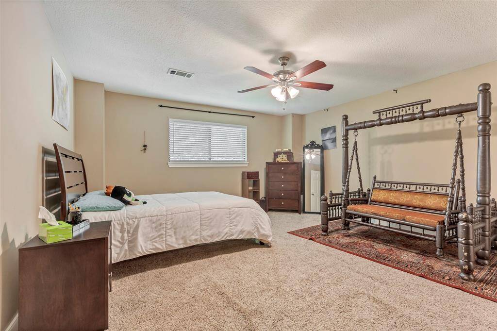 This spacious bedroom features neutral walls and carpet, a large window providing natural light, a ceiling fan, and ample space for furniture.