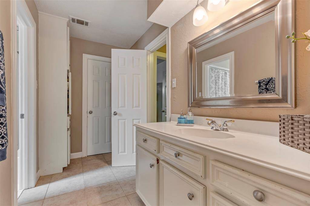 This bathroom features a spacious vanity with a large mirror, elegant lighting, and neutral tile flooring. A clean, bright design offers a welcoming and functional space.