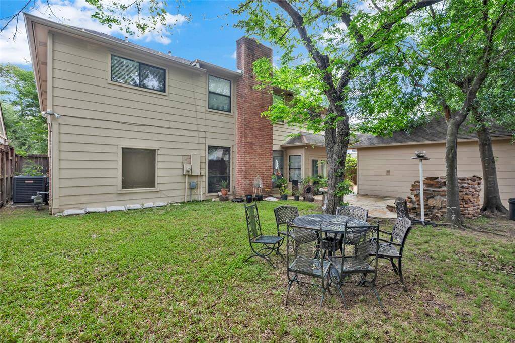 This backyard features a charming stone patio with lush greenery and mature trees. A small rock waterfall adds a tranquil touch, making it an ideal space for relaxation and outdoor entertaining.
