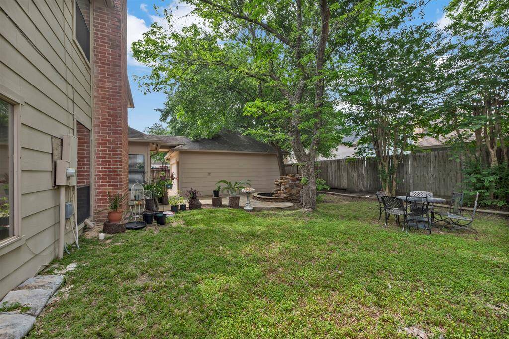 This backyard features a charming stone patio with lush greenery and mature trees. A small rock waterfall adds a tranquil touch, making it an ideal space for relaxation and outdoor entertaining.