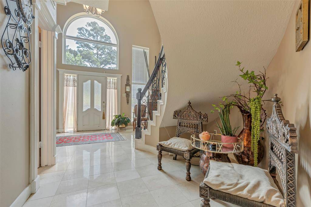 This elegant home entryway features a high ceiling with a large arched window, allowing natural light to flood the space. The polished tile floor adds a touch of luxury, while a curved staircase with ornate railings leads to the upper level.