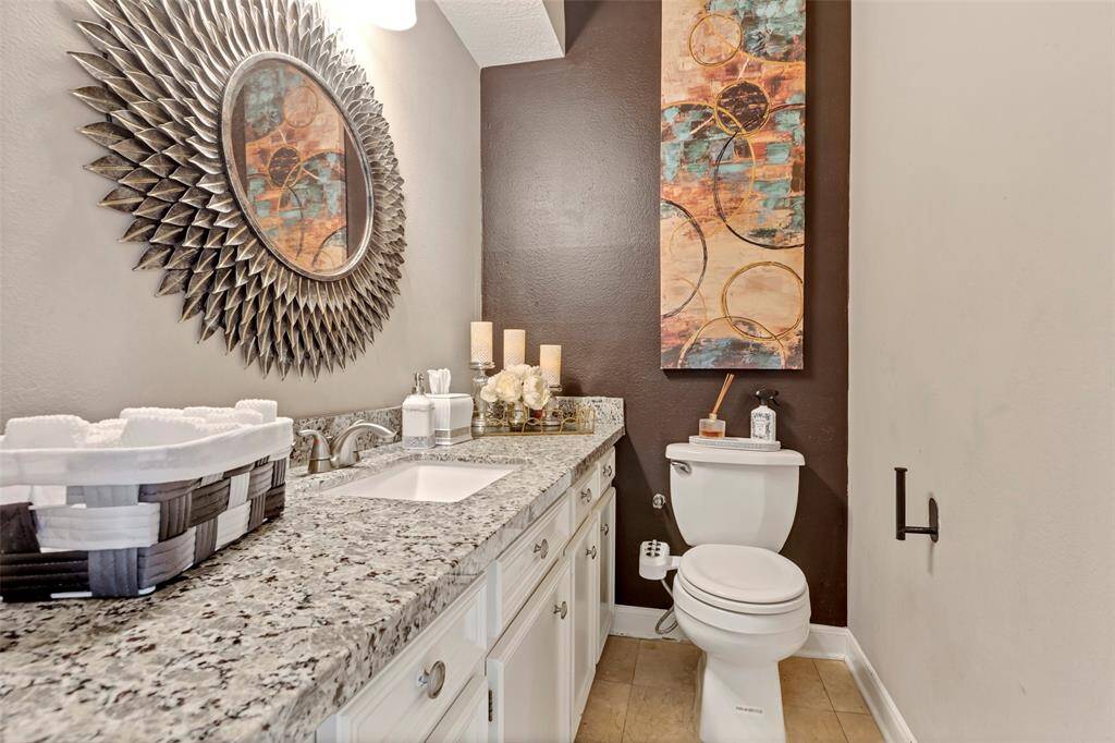 This bathroom features a stylish granite countertop with a modern sink, decorative mirror, and contemporary artwork. The neutral tones and elegant decor create a welcoming and sophisticated atmosphere.