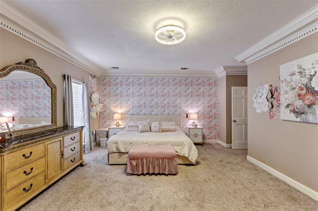 This spacious bedroom features a cozy, carpeted floor and elegant crown molding. Soft lighting and tasteful decor create a warm and inviting atmosphere.