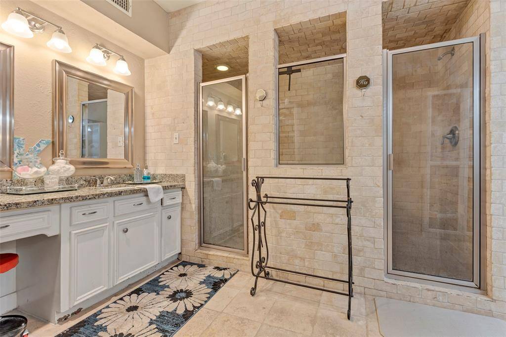 This bathroom features a spacious shower with double glass doors and brick-style tiling. It includes a double vanity with granite countertops and ample cabinet storage. The room is well-lit with modern fixtures and has a neutral palette for a clean, timeless look.