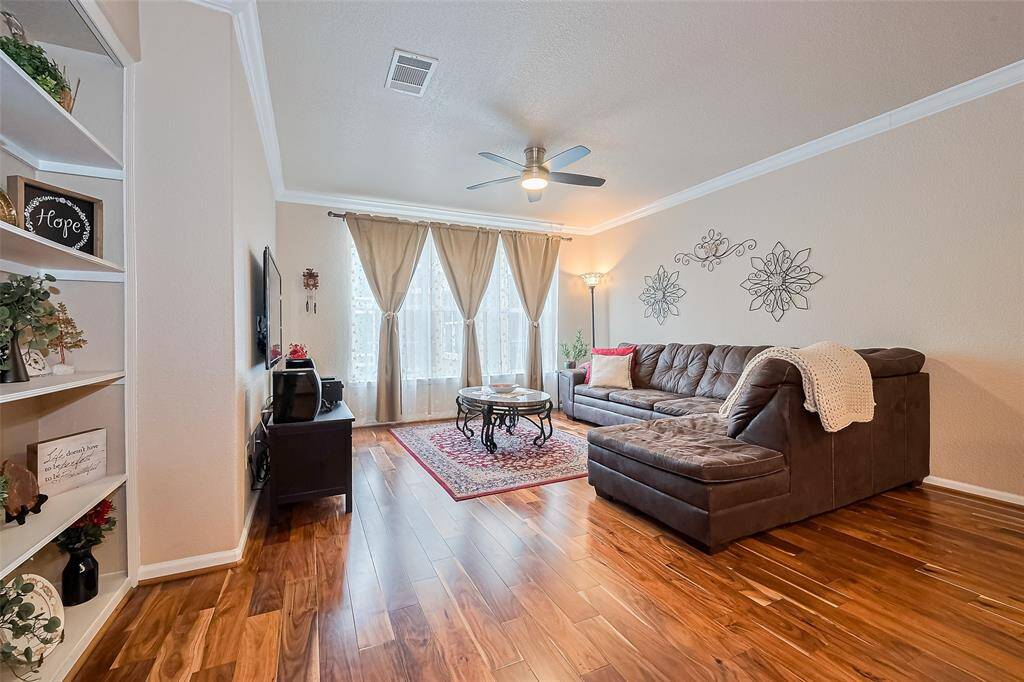 Spacious and full of natural light, the living room features rich wood flooring and large windows. A ceiling fan offers comfort, while a recessed built-in shelf adds architectural interest and practical display space.