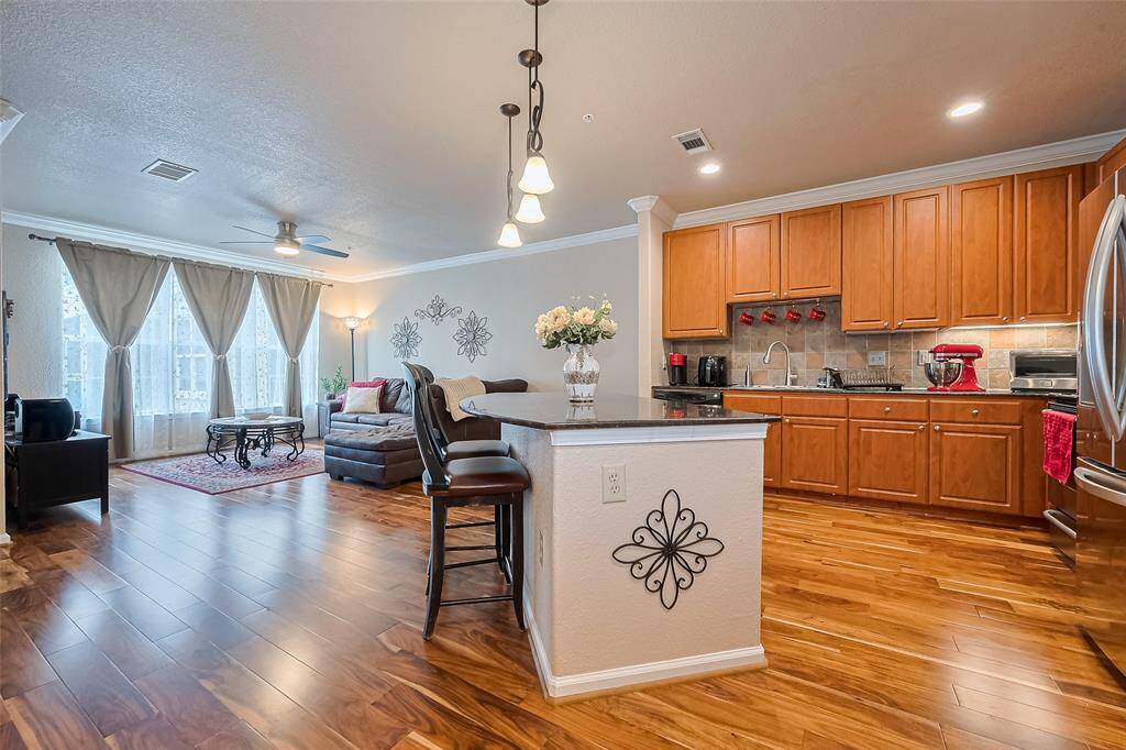 The expansive kitchen features abundant cabinetry, a central island with bar seating, tasteful backsplash, and layered lighting from pendants and recessed fixtures.