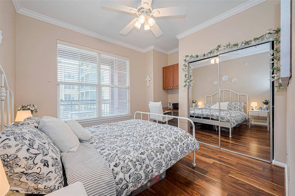 This bedroom includes mirrored closet doors, a large window, and a ceiling fan. A tucked-away corner workstation with desk and overhead cabinetry adds functionality without clutter.